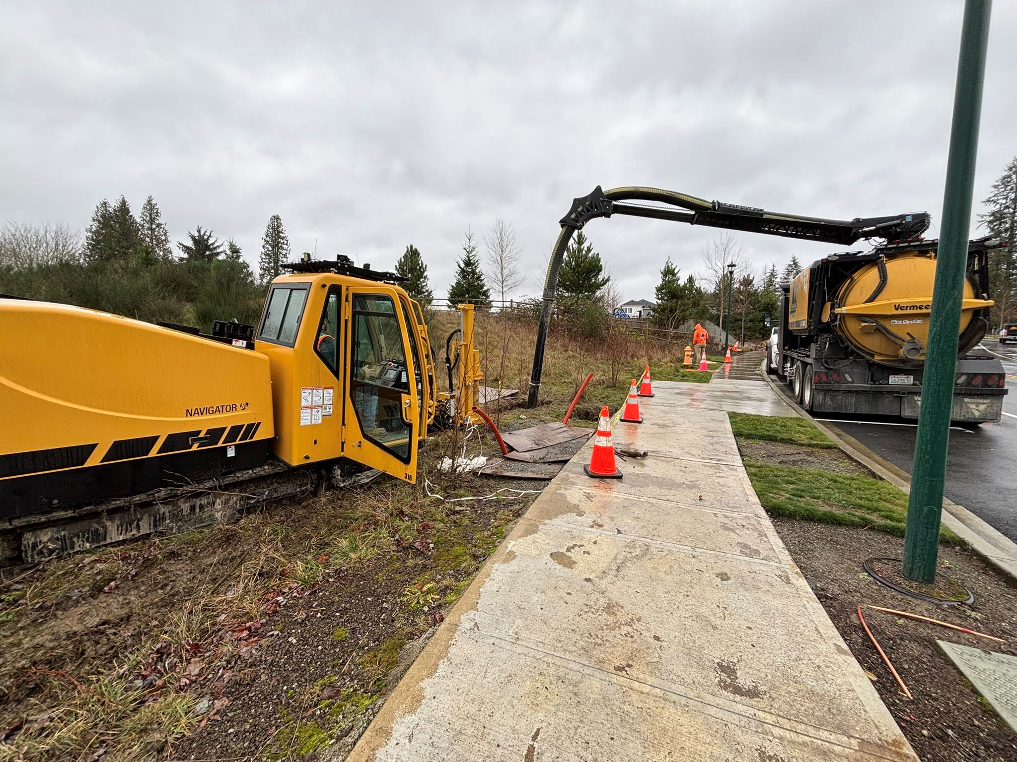 A construction crew next to the sidewalk is installing fiber using a directional drilling machine.