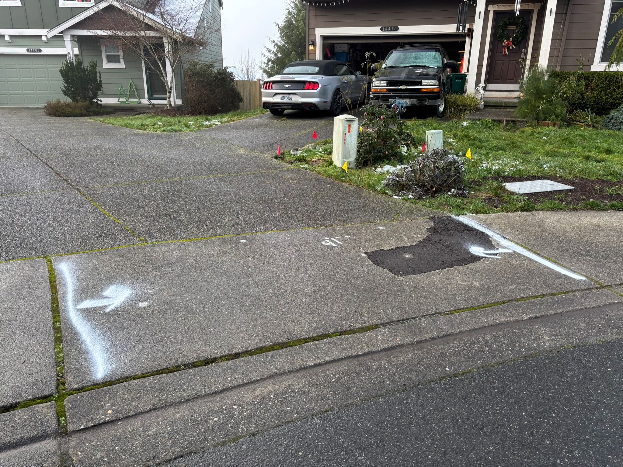 Concrete sidewalk panel with temporary asphalt patch and painted white arrows.